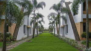 A courtyard with a central lawn, surrounded by buildings with white and brown facades, and palm trees. - Pai Resorts (Belagavi)