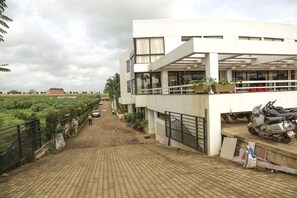 A modern building with a paved walkway, a parked scooter, and potted plants. - Pai Resorts (Belagavi)