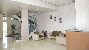 A modern lobby with a reception desk, two sofas, a staircase, and a potted plant. - Pai Resorts (Belagavi)