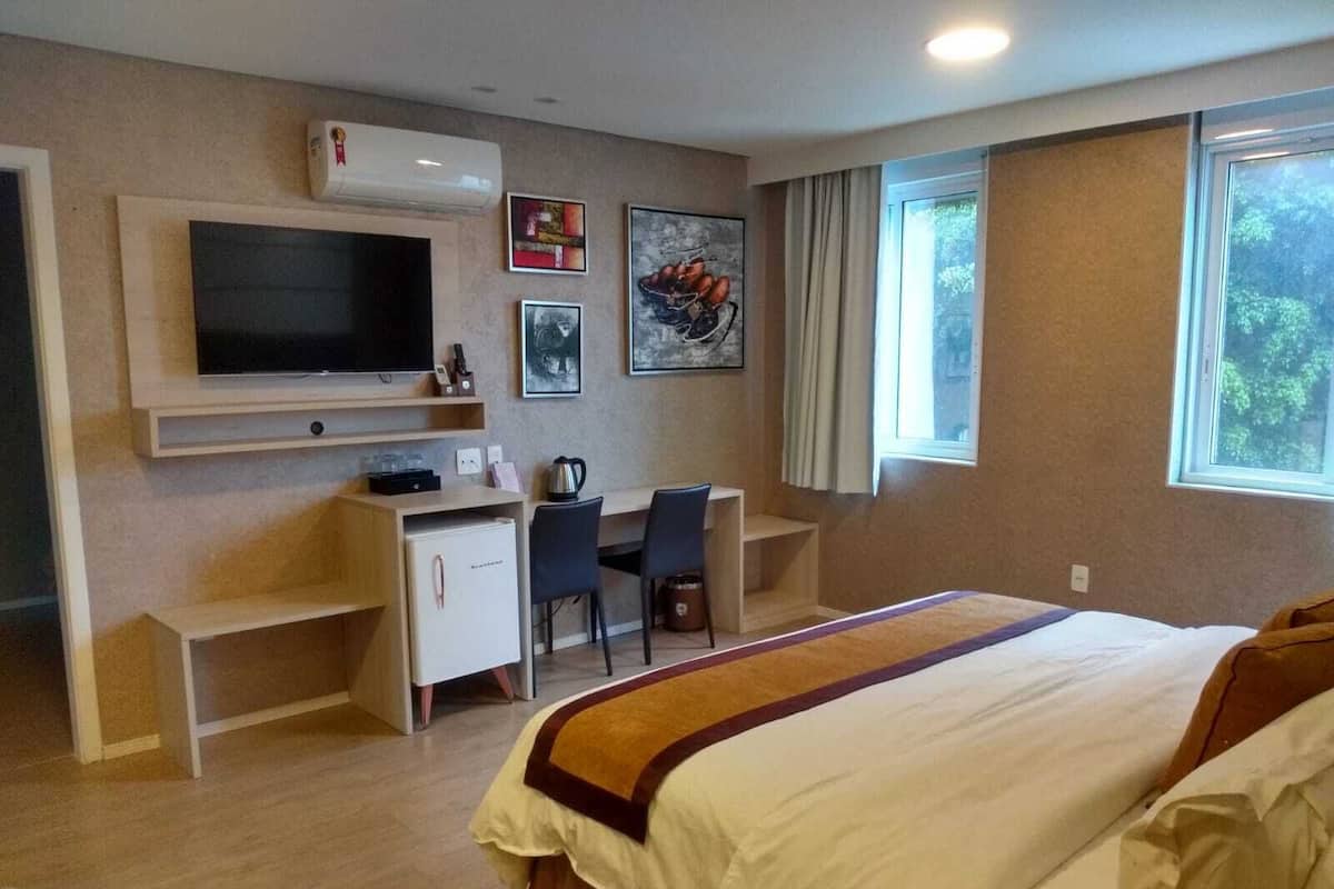 A hotel room with a bed, a desk, a television, and a window.