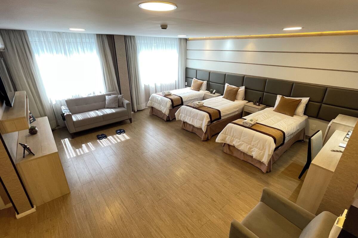 A hotel room with two single beds, a sofa, a desk, and a TV.