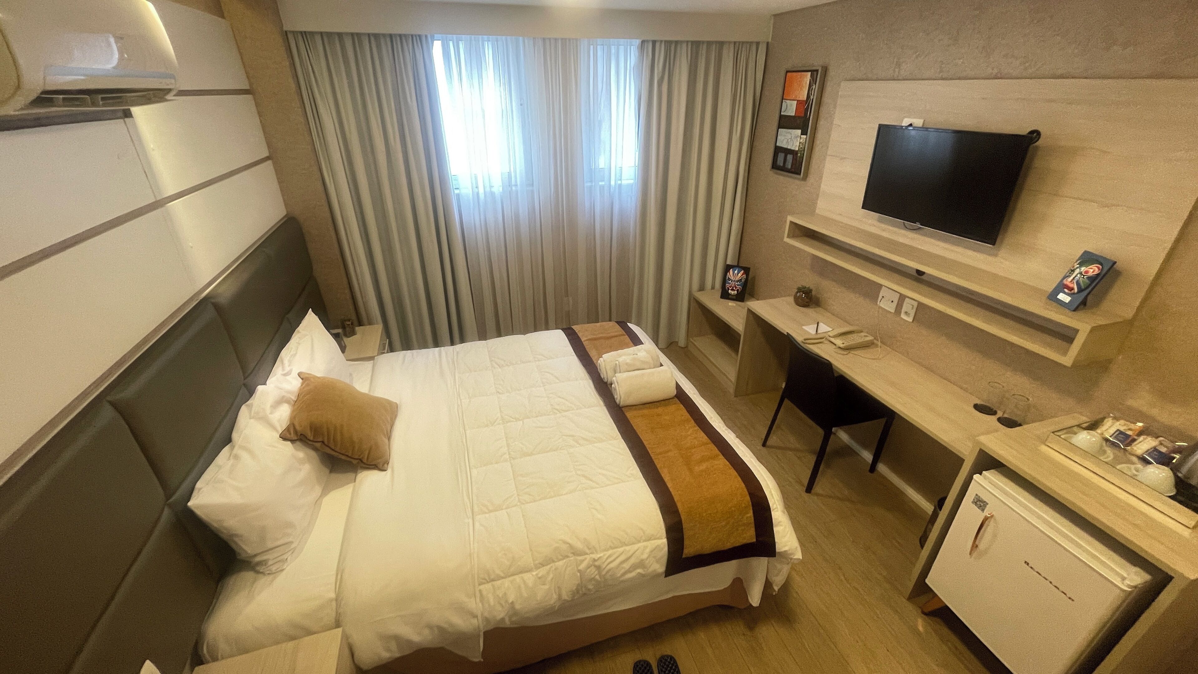 A hotel room with a bed, a desk, a television, and a minibar.