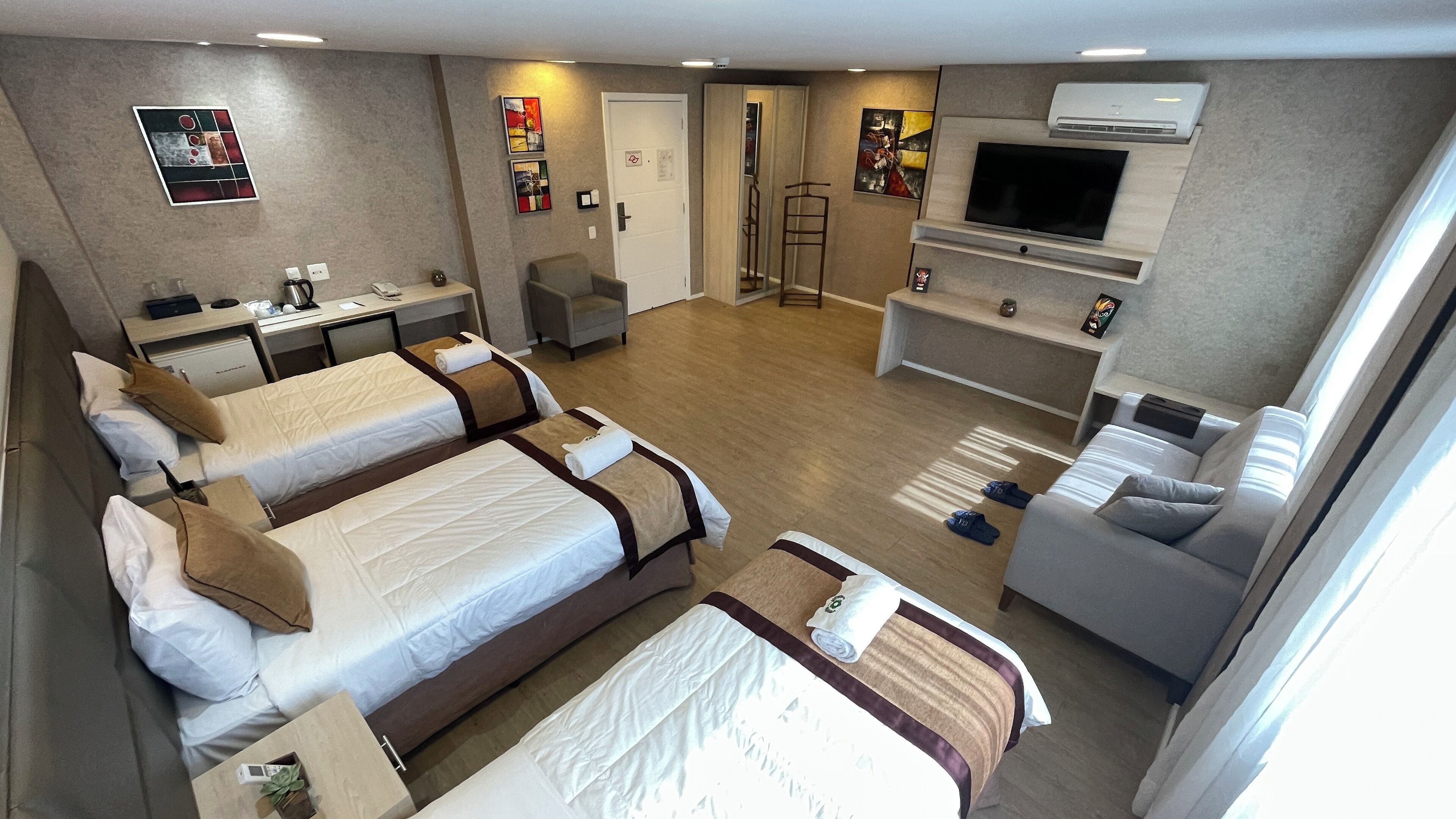 A hotel room with a large bed, a smaller bed, a sofa, a desk, and a TV.