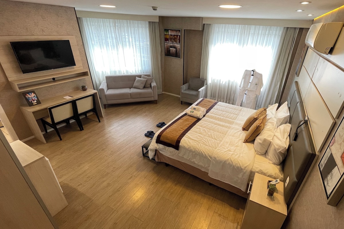 A hotel room with a large bed, a desk with a flat-screen TV, a sofa, and a chair.