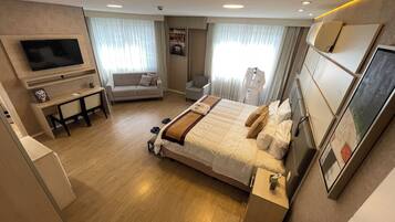 A hotel room with a large bed, a desk with a flat-screen TV, a sofa, and a chair.