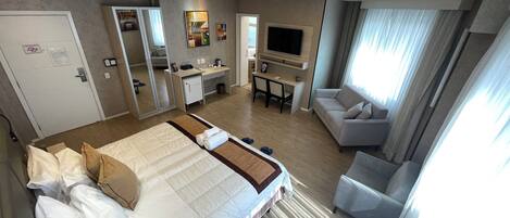 A hotel room with a large bed, a desk, a TV, and a seating area.