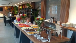 A buffet setup with various food items and a beverage station, surrounded by chairs and tables.