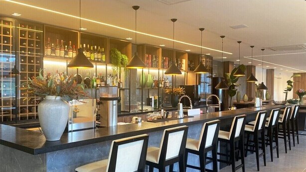 A modern bar area with a long counter, multiple hanging pendant lights, and a variety of bar tools and bottles.