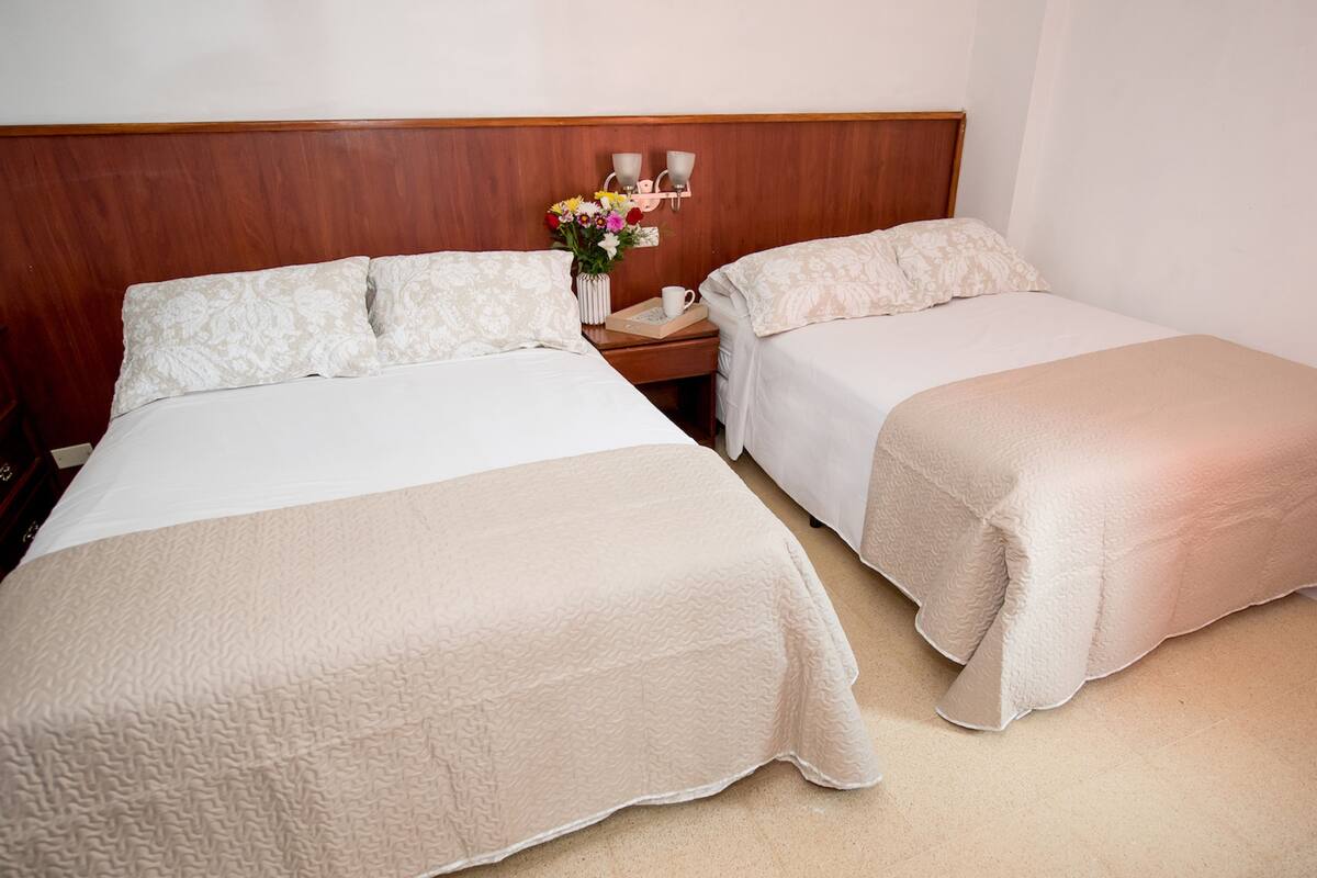 A hotel room with two beds, a nightstand with a vase of flowers, and a wooden headboard.