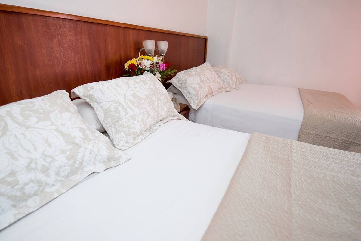 A hotel room with two beds, a wooden headboard, and a bedside table with a vase of flowers.