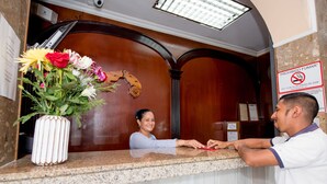 A reception desk with a vase of flowers, a no-smoking sign, and a wooden interior. - Hotel Acapulco (Panama City)