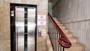 An elevator with a metallic interior, adjacent to a staircase with a wooden handrail and beige steps. - Hotel Acapulco (Panama City)