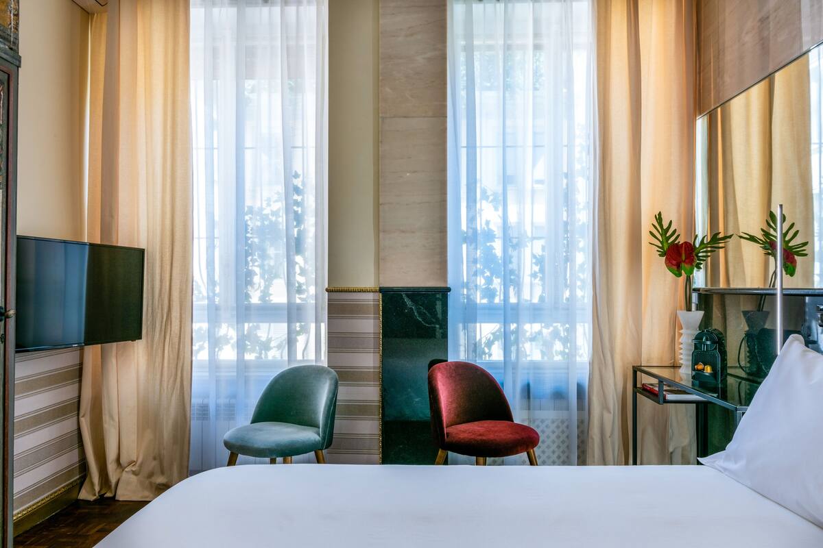 A hotel room with a bed, two chairs, a TV, and a mirror.