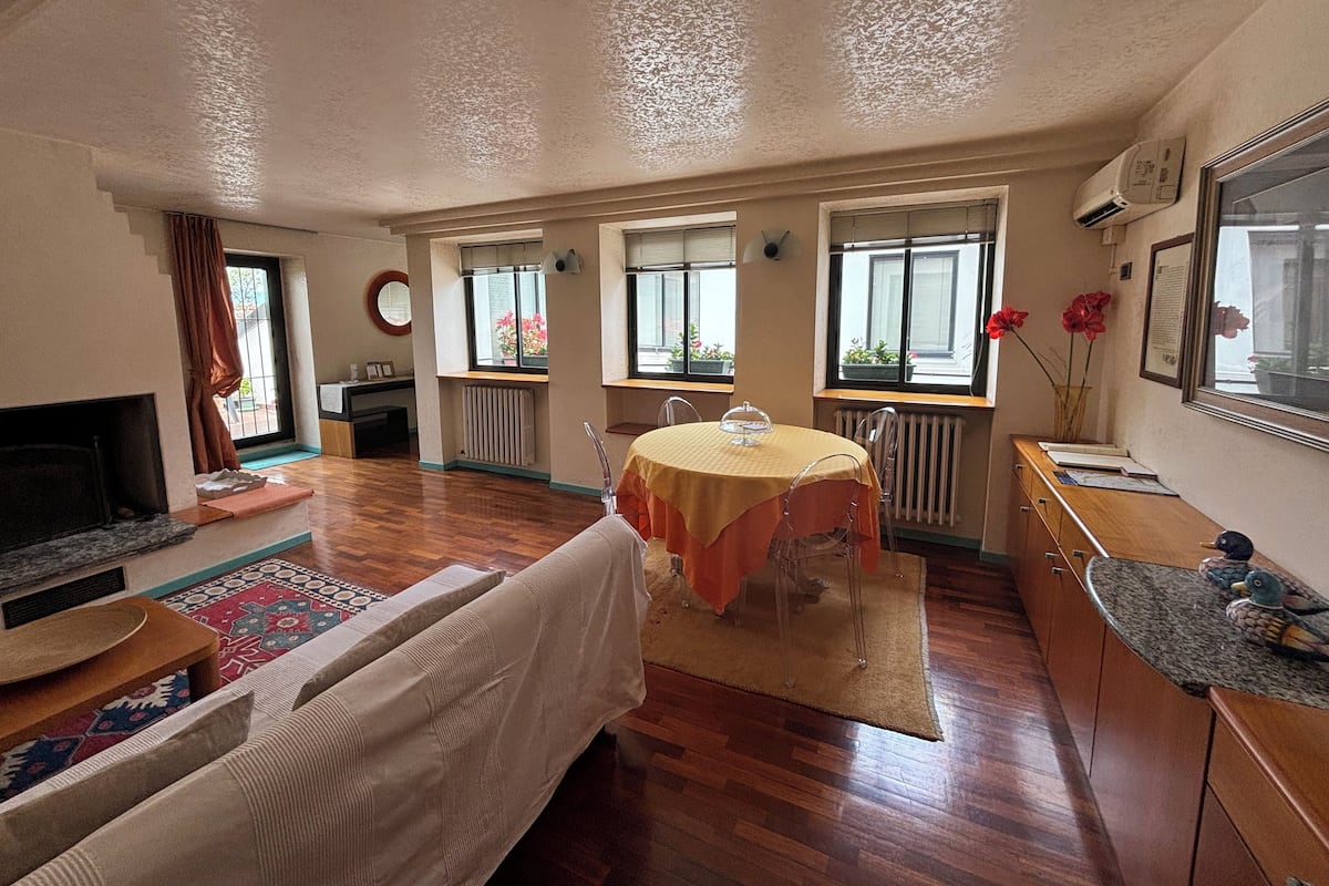 A spacious living room with a fireplace, a dining table with chairs, and large windows with flower boxes.