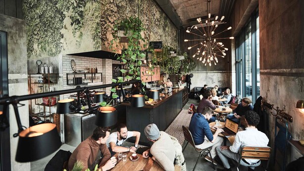Un café moderno con pared de ladrillo rústica, plantas colgantes y una zona de bar central.