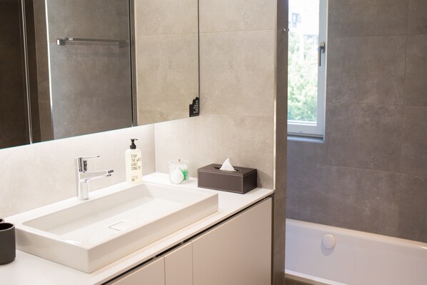 Ein modernes Badezimmer mit einem großen Waschbecken, einem Spiegel, einem Handtuchspender und einer Badewanne.