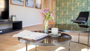 Una sala de estar moderna con una mesa de centro de vidrio, un jarrón con flores, un periódico y un control remoto.