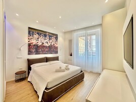 Una camera da letto moderna con un letto grande, un quadro di fenicotteri, una TV e una finestra con tende leggere.