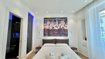 Een moderne hotelkamer met een groot bed, een flamingo schilderij, een inloopkast en een badkamer met een glazen deur.