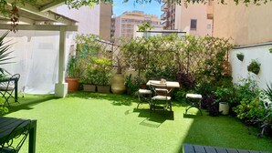 A patio with artificial grass, a table and chairs, potted plants, and a pergola. - J&O' Luxury Suite (Cagliari)