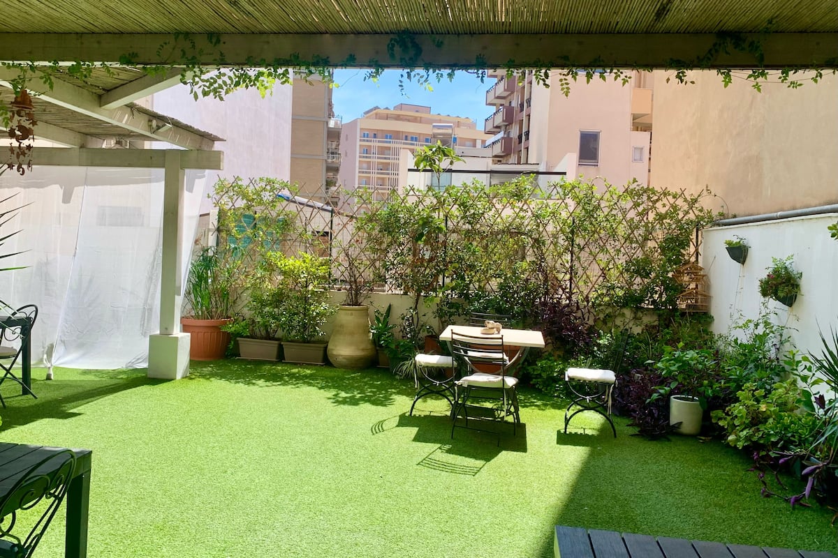 A patio with artificial grass, a table and chairs, potted plants, and a pergola.