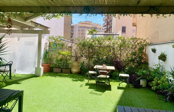 A patio with artificial grass, a table and chairs, potted plants, and a pergola. - J&O' Luxury Suite (Cagliari)