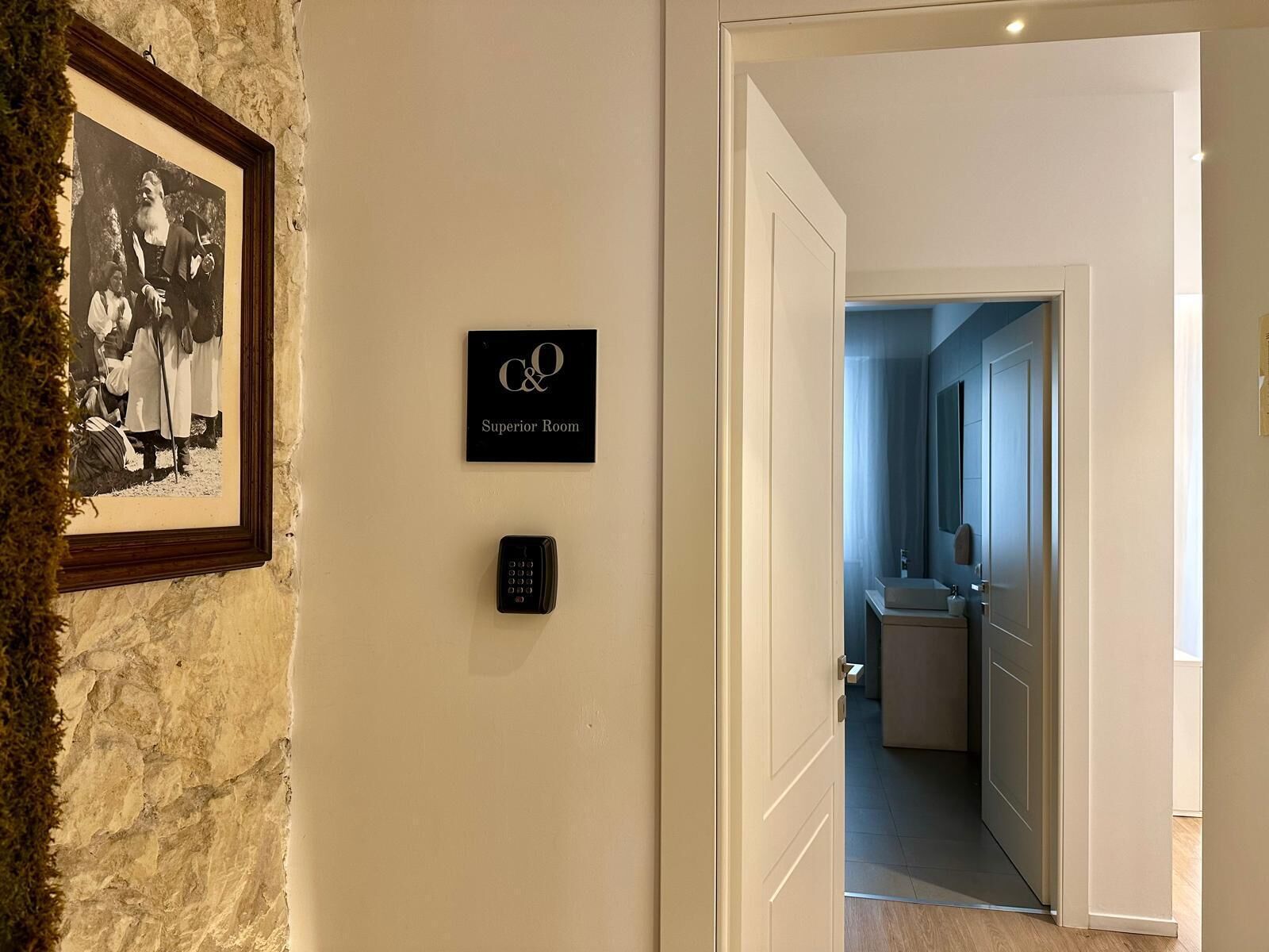 Ein Flur mit einem gerahmten historischen Foto, einem Schild für das „Superior Room“ und einer modernen Tür zu einem Badezimmer.
