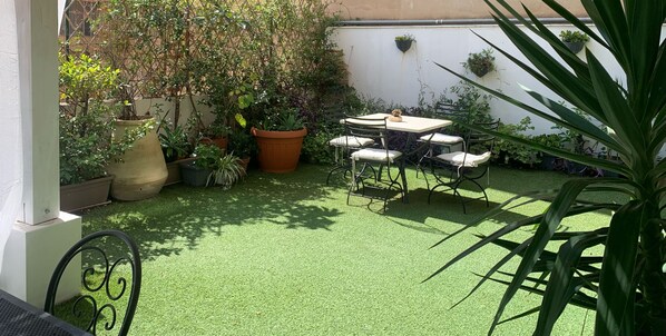 Un espace patio aménagé avec une table et des chaises, entouré de plantes en pot et recouvert d’un gazon artificiel vert.
