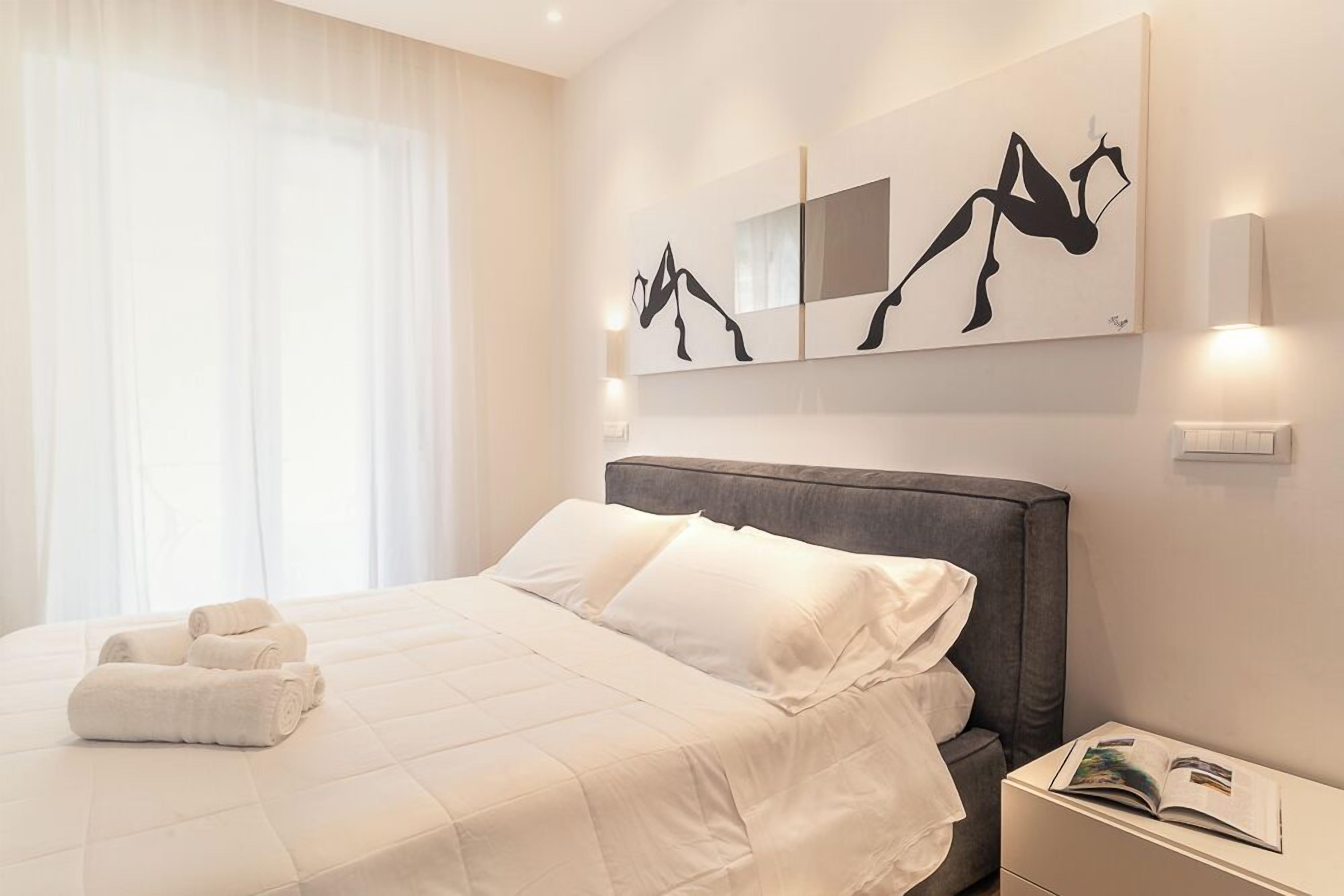 Une chambre d’hôtel avec un lit, une table de chevet sur laquelle se trouve un livre, et des œuvres d’art abstraites accrochées au mur.
