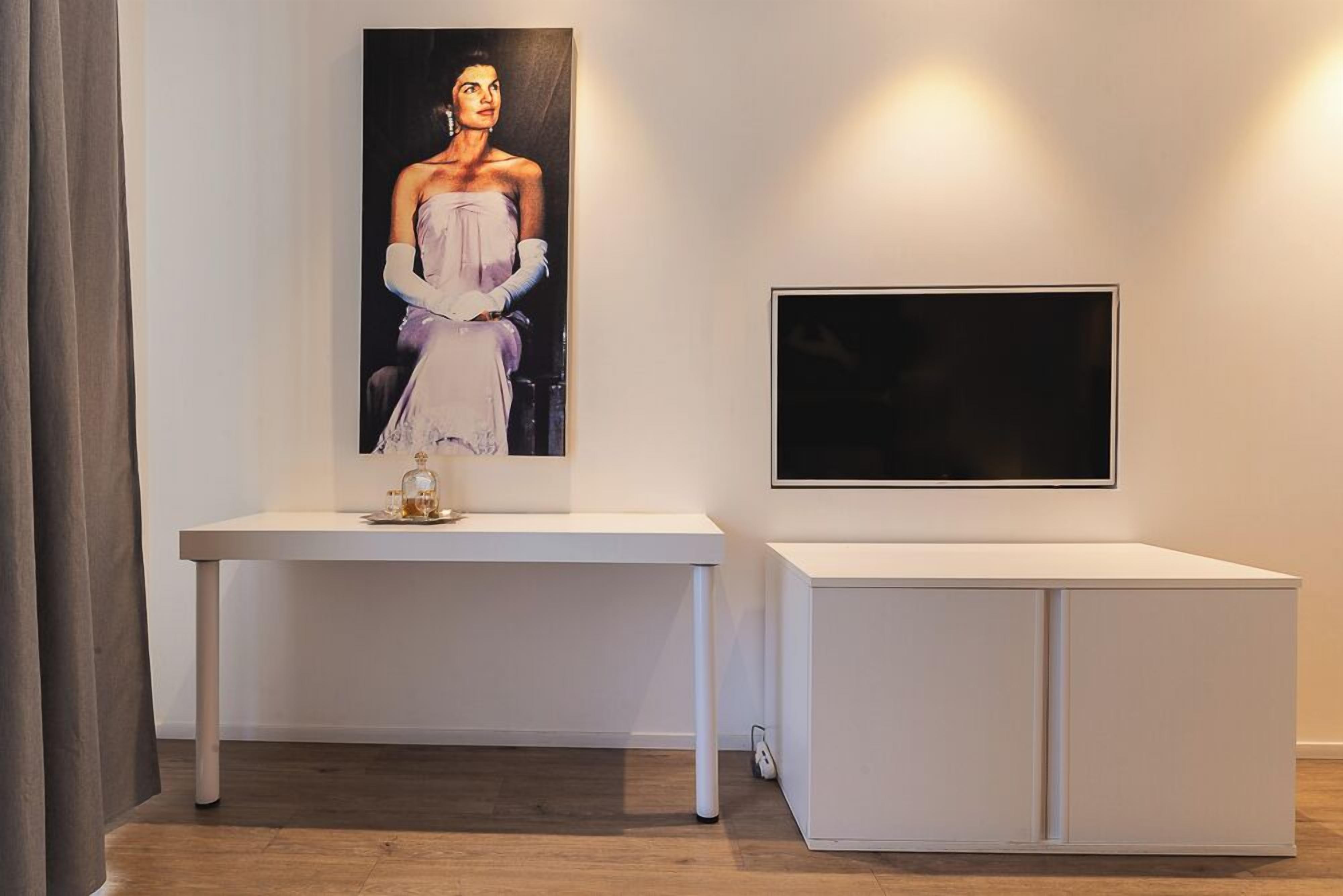 Une pièce au décor minimaliste, avec une table blanche, un portrait encadré et un téléviseur à écran plat.