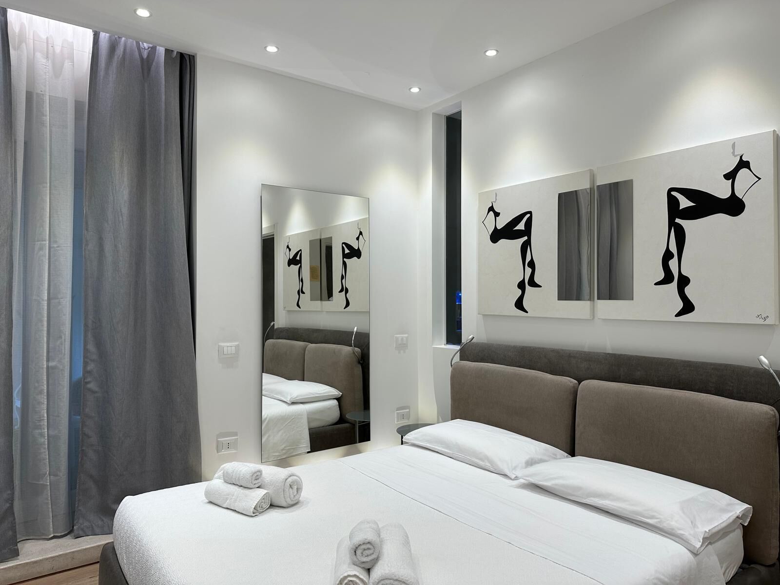 Ein modernes Hotelzimmer mit einem großen Bett, einem Spiegel und Kunstwerken an den Wänden.
