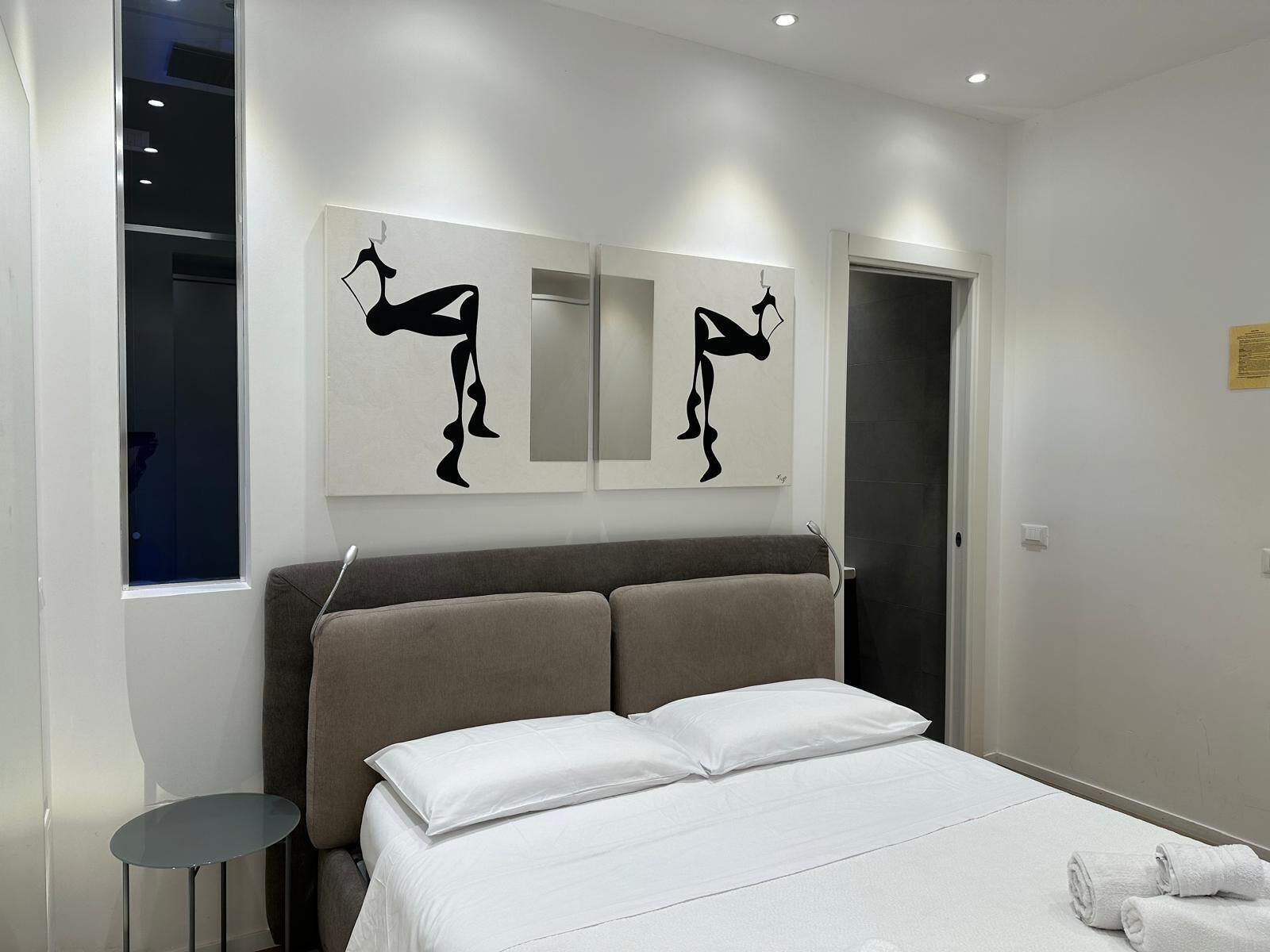 Ein modernes Hotelzimmer mit einem großen Bett, einem kleinen Nachttisch und zwei abstrakten Wandbildern.