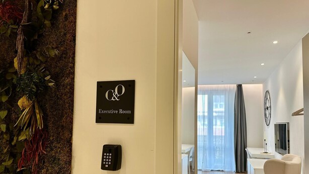 A modern executive room with a sign indicating its use, a wall-mounted phone, and a view into a well-lit living area with a sofa and curtains. - J&O' Luxury Suite (Cagliari)