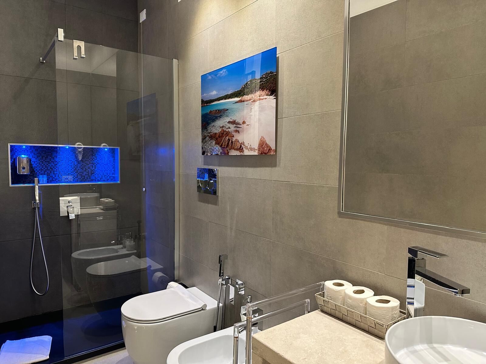 Een moderne badkamer met een douchecabine van glas, een toilet, een wastafel met spiegel en een toiletrolhouder aan de muur.