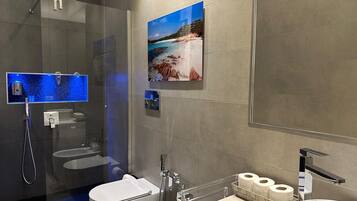 Een moderne badkamer met een douchecabine van glas, een toilet, een wastafel met spiegel en een toiletrolhouder aan de muur.
