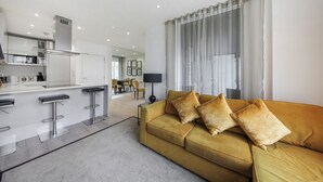 A modern living room with a sofa and a kitchen area in the background. - Lux 2 & 3 Bed Apartments in Camden Town FREE WIFI by City Stay Aparts London (London)