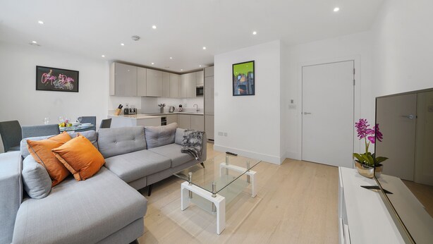 A modern living room with a grey sofa, orange cushions, a glass coffee table, and a white cabinet. - Lux 2 & 3 Bed Apartments in Camden Town FREE WIFI by City Stay Aparts London (London)