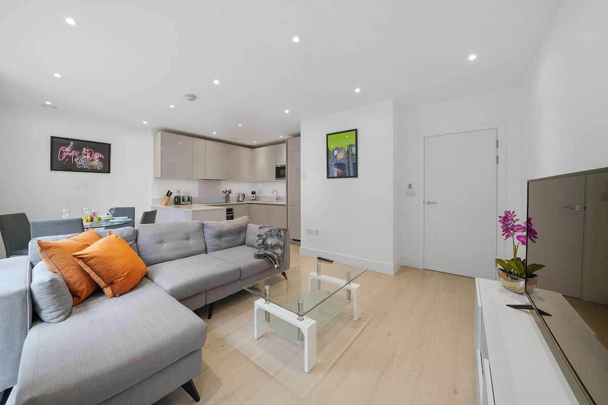Un salon moderne avec un canapé gris, des coussins orange, une table basse en verre et un meuble blanc.