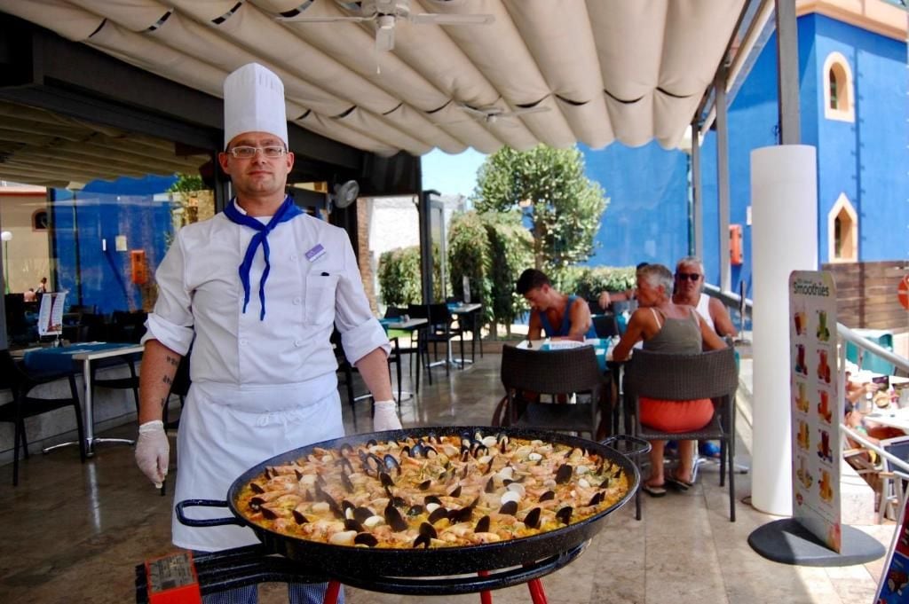Un espacio de comedor al aire libre con un chef sirviendo paella de mariscos.