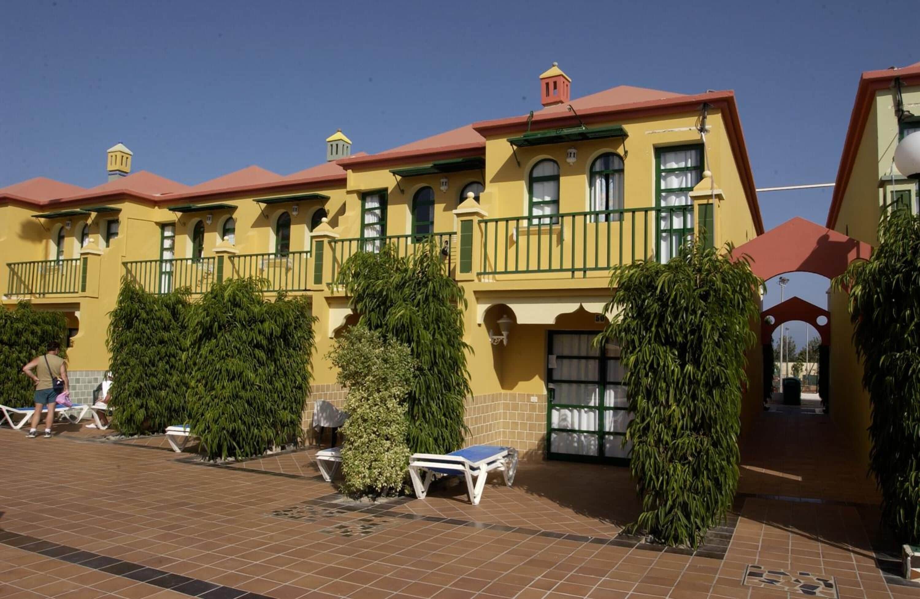 A yellow building with balconies and a tiled patio area with sun loungers.