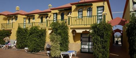 Un bâtiment jaune doté de balcons et d’une terrasse carrelée avec des chaises longues.