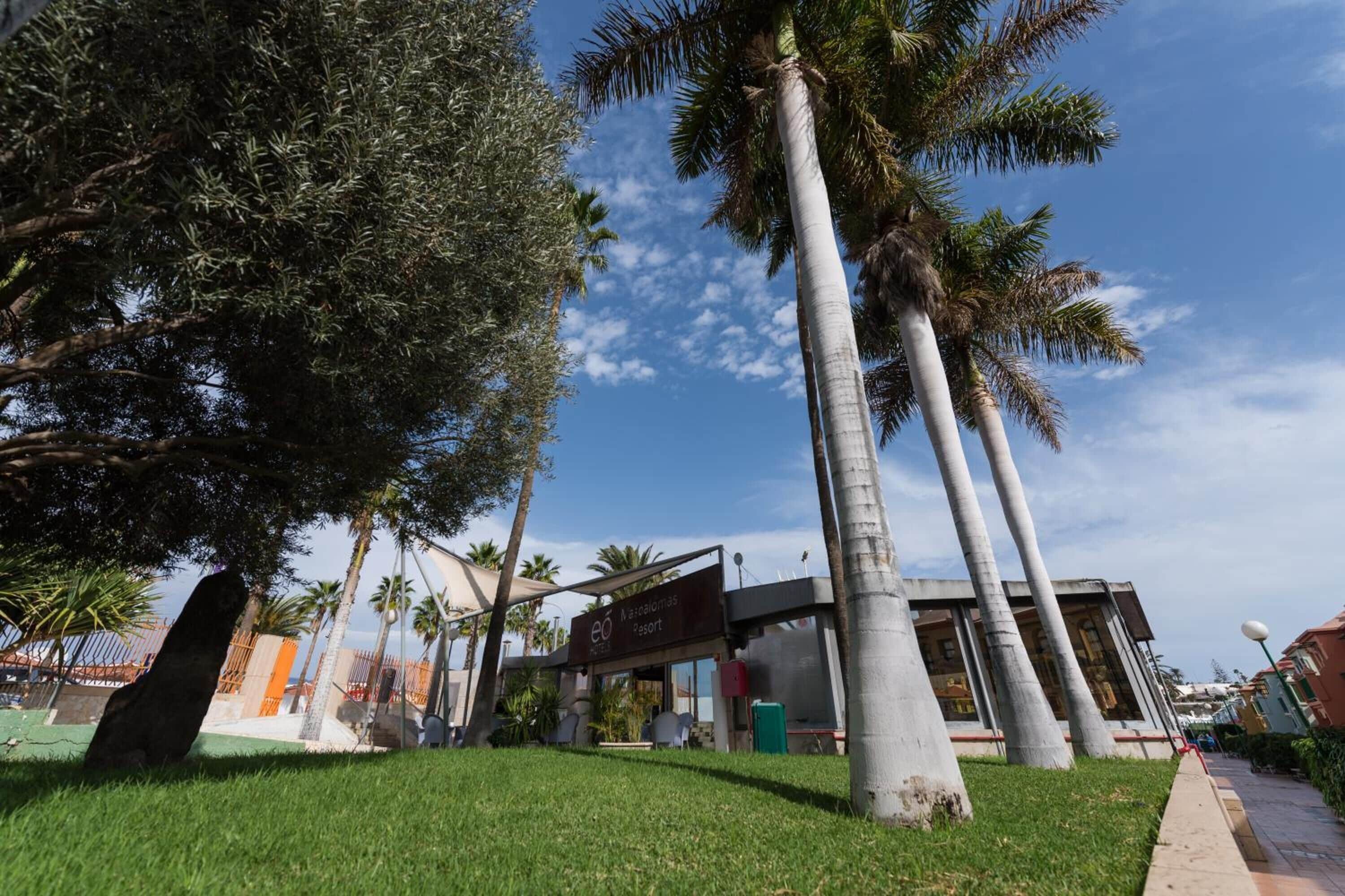 Un resort con palme, un cartello e un edificio dal design moderno.