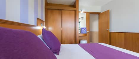 Une chambre d’hôtel avec un lit, une armoire en bois et une petite étagère contenant des articles de toilette.