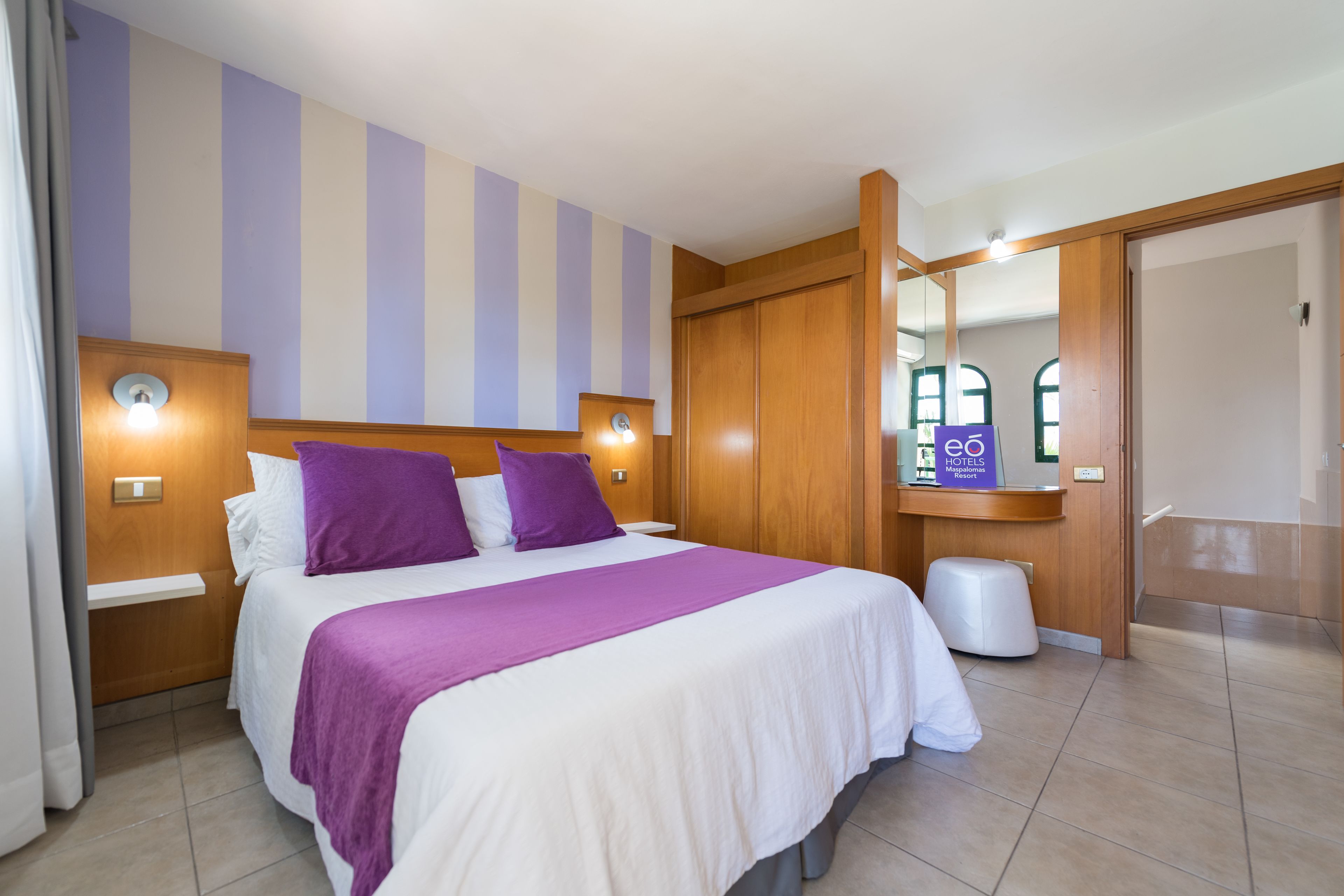 A hotel room with a large bed, wooden headboard, and a mirror above the bed.