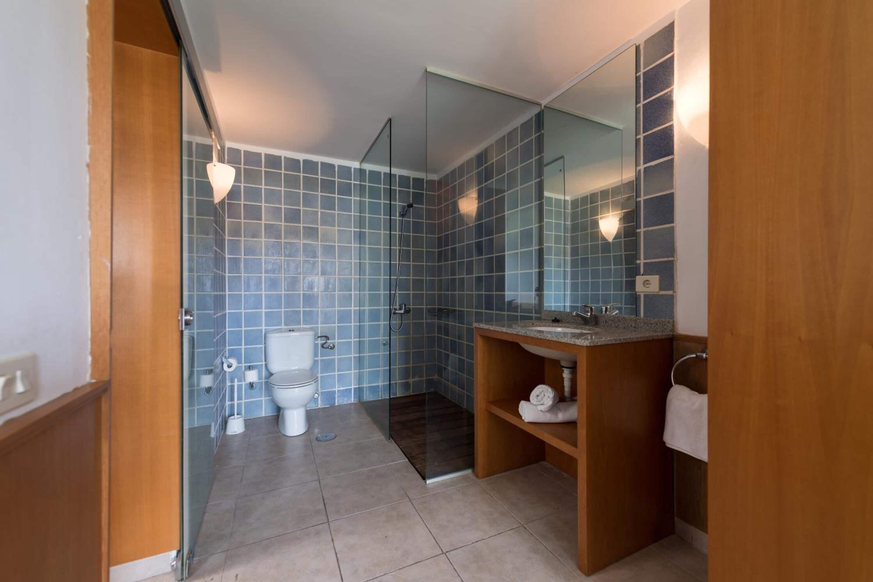 A modern bathroom with a glass shower enclosure, a wooden vanity, and a large mirror.