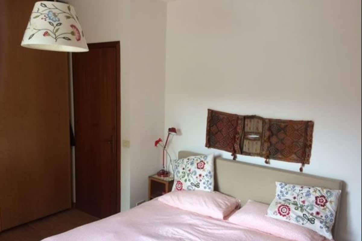 A bedroom with a bed, a nightstand, a lamp, and a wooden door.