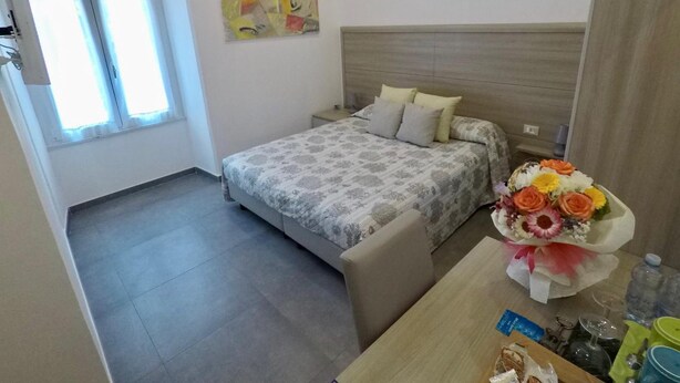 Une chambre d’hôtel avec un lit, un bureau agrémenté d’un bouquet de fleurs, un tableau au mur et une fenêtre avec des rideaux.