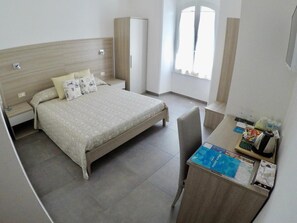 Un dormitorio con cama, escritorio, silla, armario y ventana.