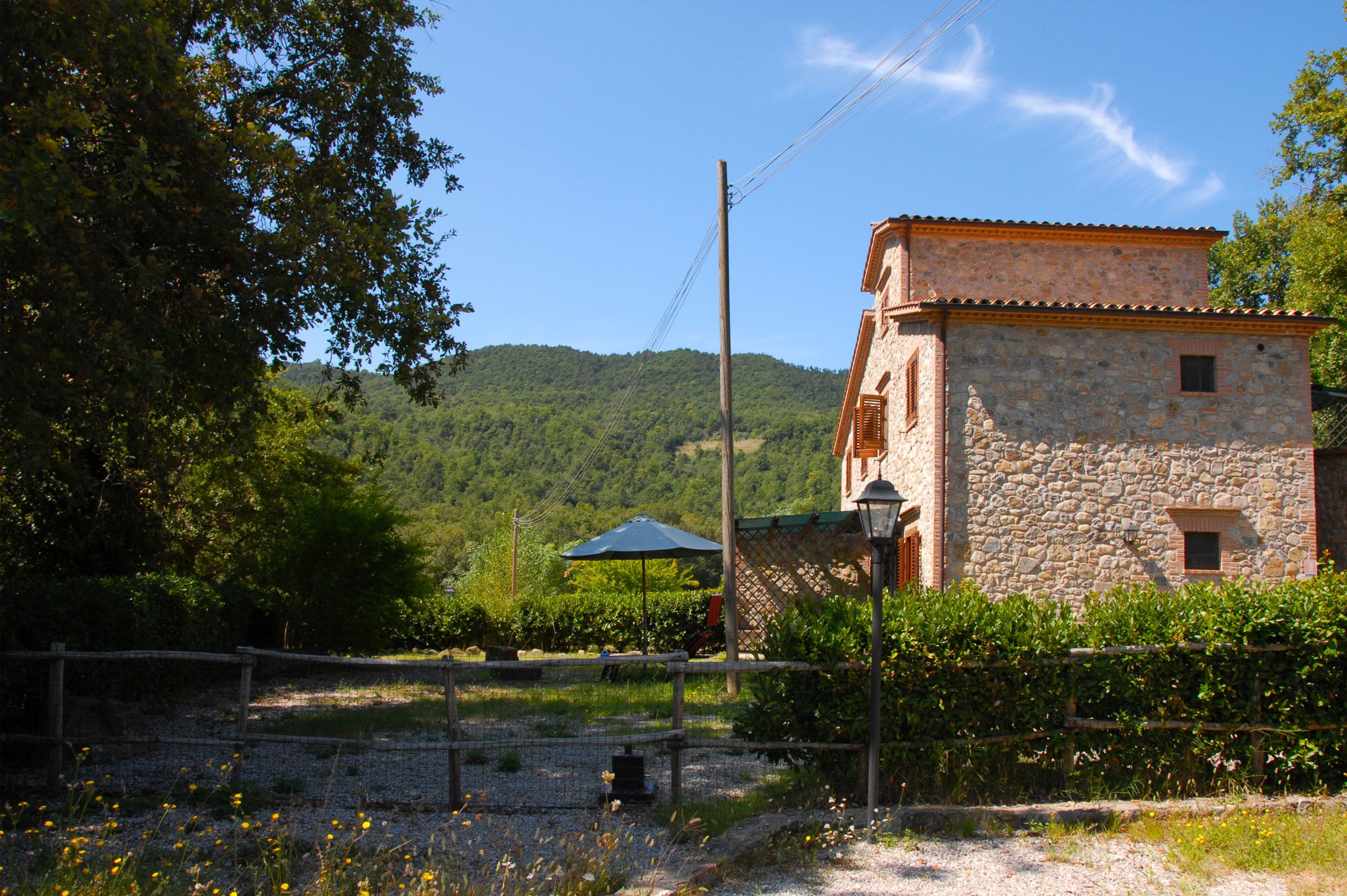 Un bâtiment en pierre, doté d’un toit en tuiles, entouré de verdure et surplombé d’un ciel dégagé.