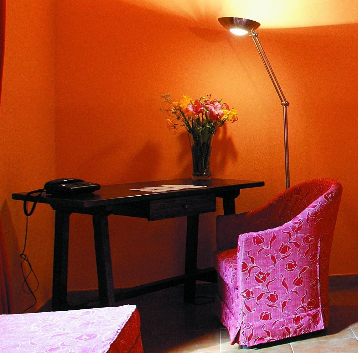 A room with a desk, a chair, a lamp, and a vase with flowers.